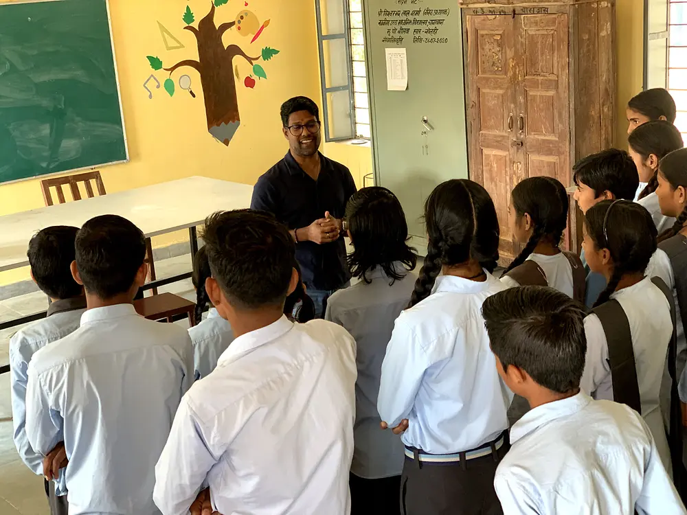 A volunteer speaking to a group of students in a classroom during a community activity in India.
