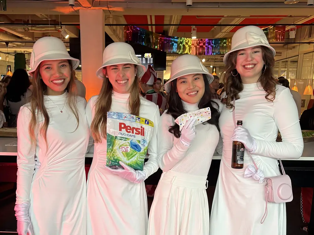 Four employees in coordinated white outfits holding Persil products at themed event with colorful decorations