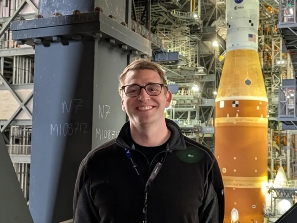 Employee standing inside aerospace facility with NASA Artemis rocket displayed in the background