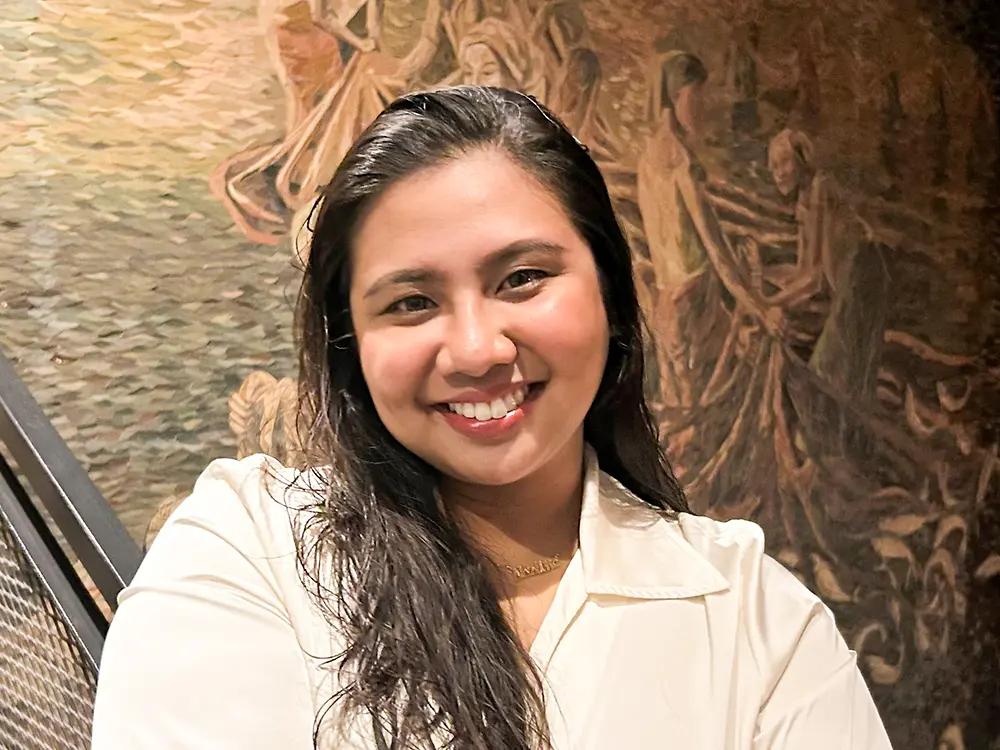 
Recruitment partner from North America wearing a black top, standing against a light beige background, sharing advice on how to craft a successful career. 