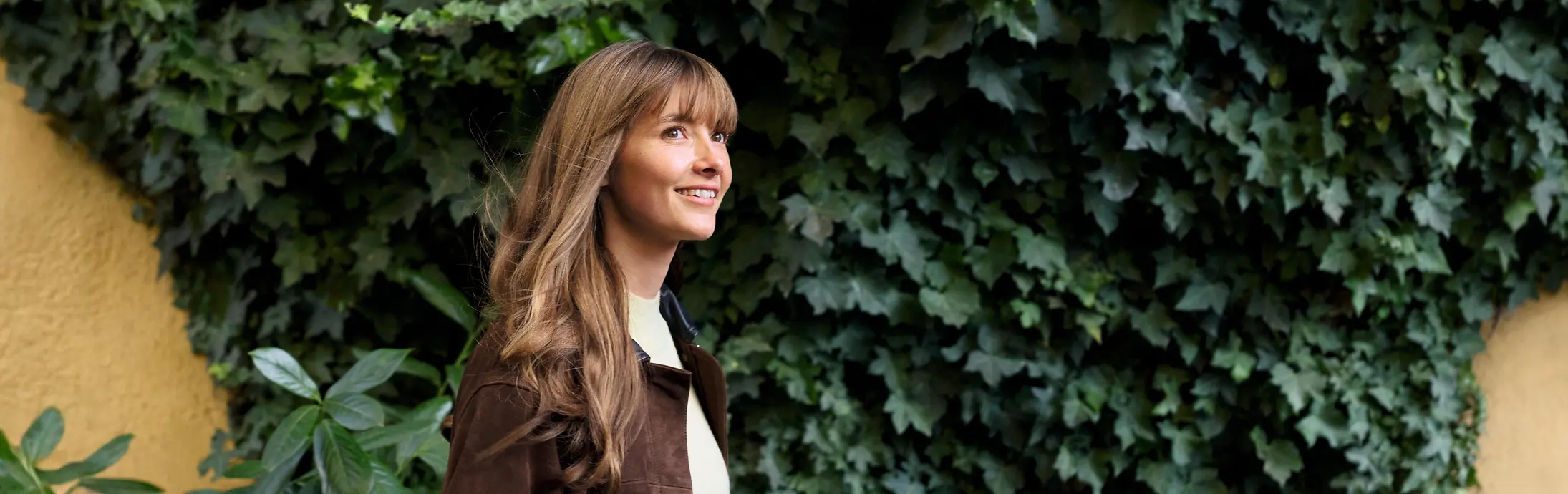 A woman walking in front of a wall covered in green plants.