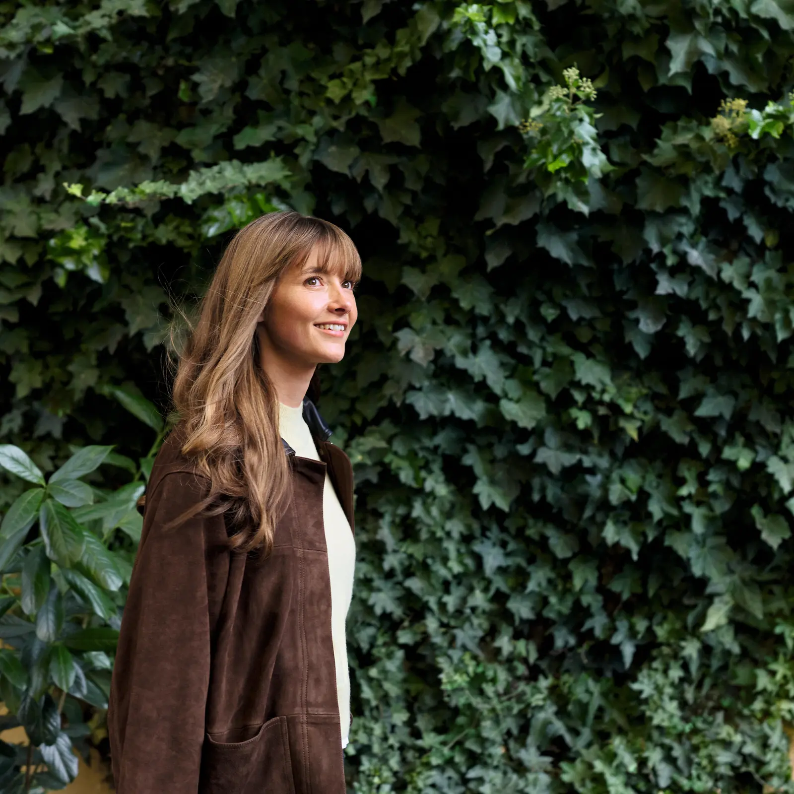 A woman walking in front of a wall covered in green plants.
